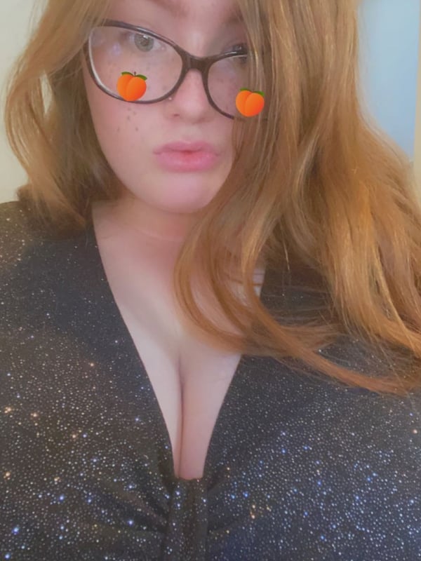 Close-up selfie of a woman with glasses and orange Snapchat filters, wearing a sparkly black top, against a plain background.