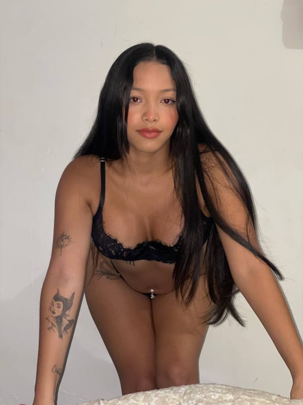 Woman with long dark hair posing confidently in lace lingerie against a plain background.