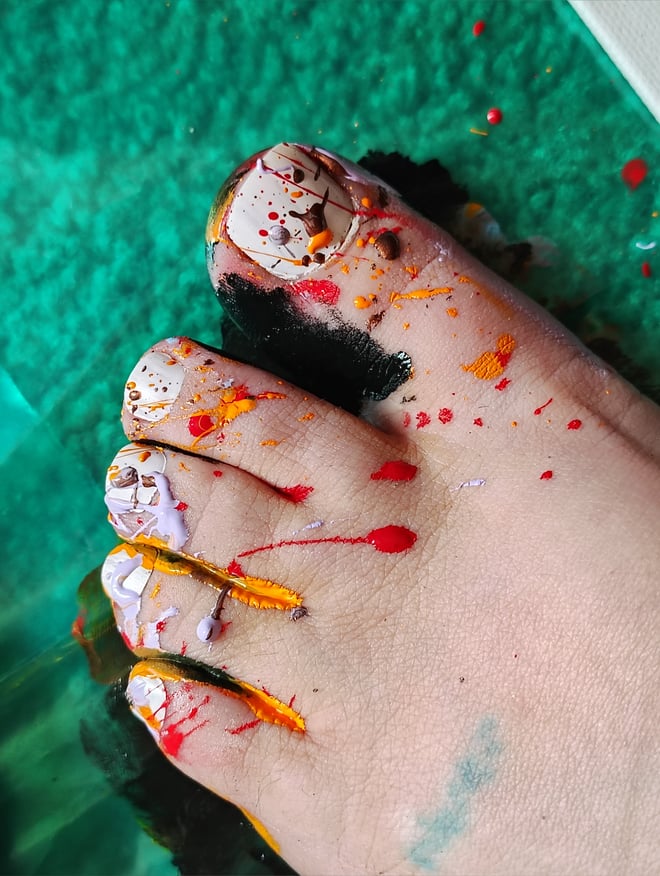 Close-up of bare feet with colorful painted toenails and artistic paint splatters on a green background.