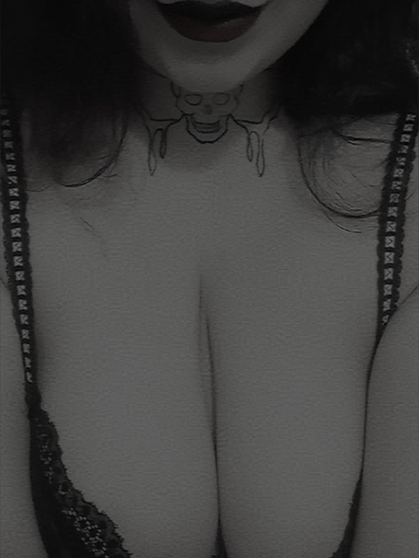 Close-up portrait of a woman with dark hair and dark lipstick, wearing a choker and lace top, smiling softly.