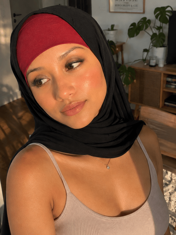 A close-up selfie of a woman wearing a hijab, posing indoors with her hand near her face.