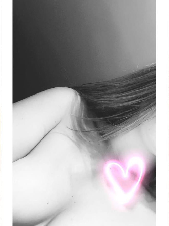 A woman with long hair lying on her side in a dimly lit setting, with a glowing pink heart effect near her chest.