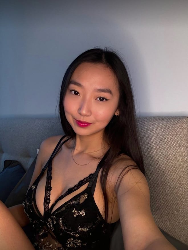 A young woman with long dark hair sitting on a bed wearing a black lace top and matching bottoms.