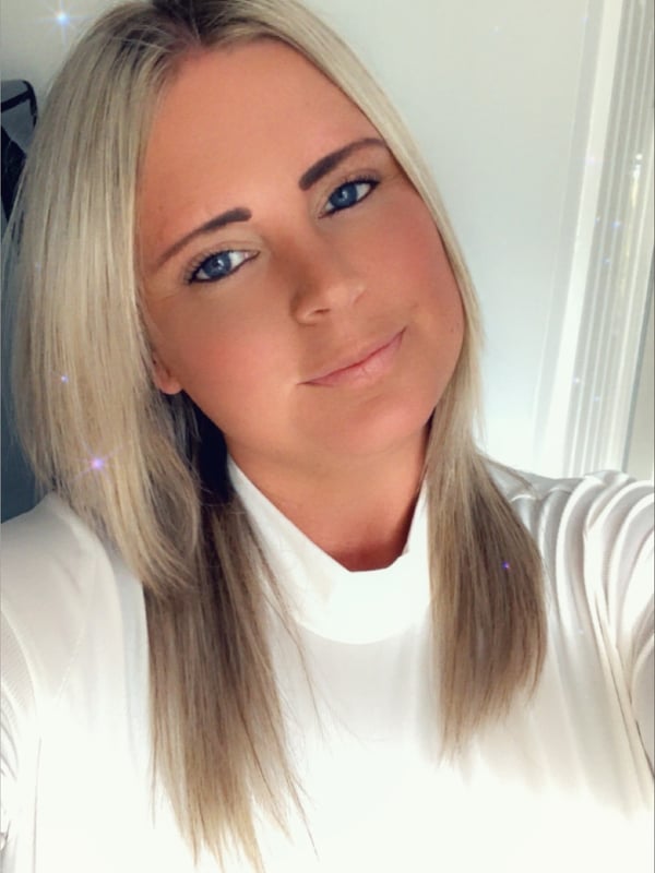 A blonde woman in a white turtleneck top smiling at the camera indoors with sparkles.