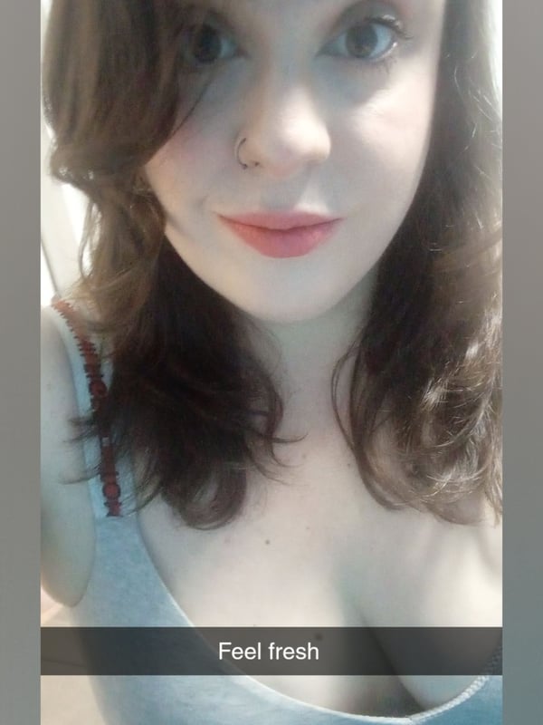 Close-up selfie of a woman with wavy brown hair, nose piercing, and red lips wearing a gray top.