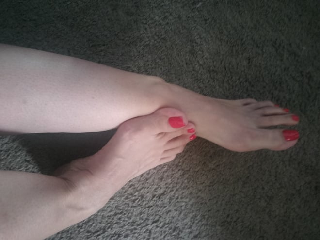 Close-up view of a person's bare legs and feet with red pedicure, posed on a carpeted floor.