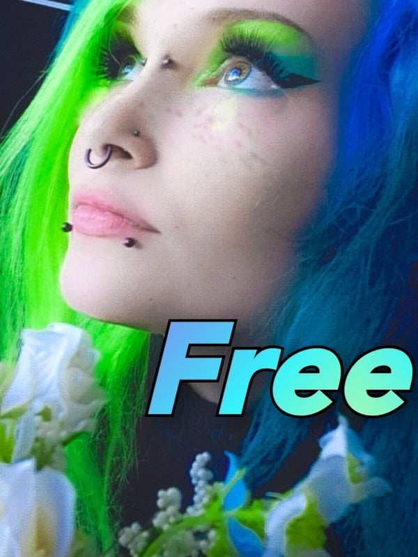 Close-up portrait of a person with vibrant green and blue hair, floral decorations, and bold makeup, featuring the word 'Free' overlay.