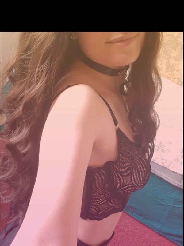 Close-up of a woman with long brown hair wearing a black choker and lace top against a teal background.