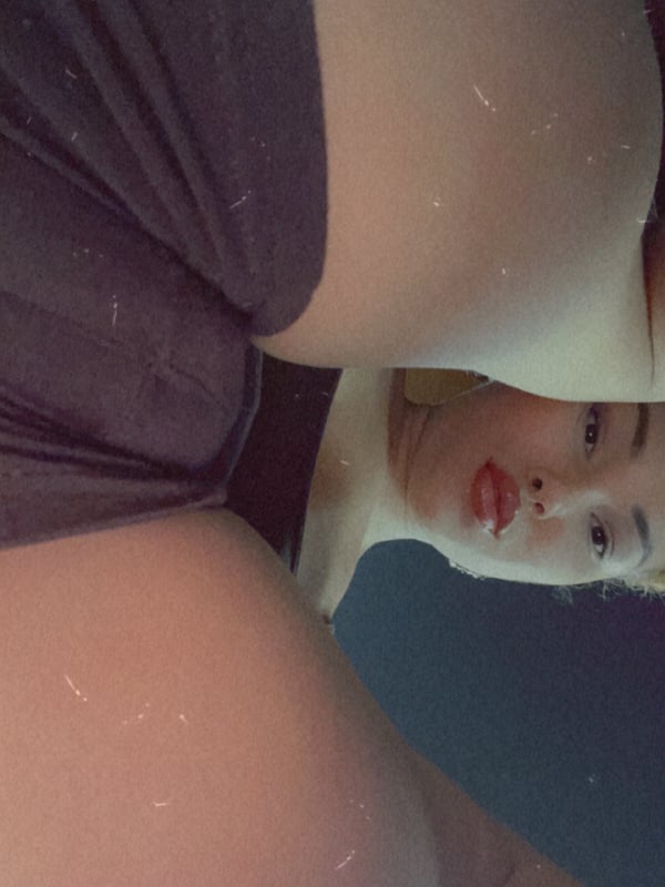 Close-up selfie of a woman with blonde hair puckering her lips, wearing dark clothing, taken in a mirror.