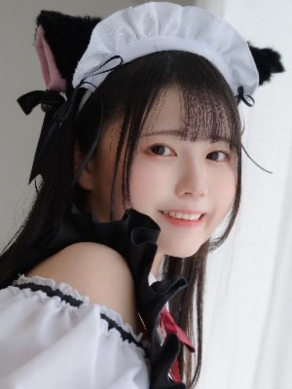 Young woman smiling in a frilly maid outfit with cat ears and headband against a plain background.
