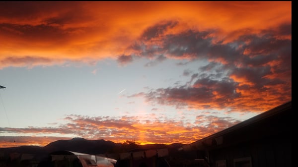 Vibrant sunset sky with orange and red clouds over a desert landscape featuring mountains and buildings.