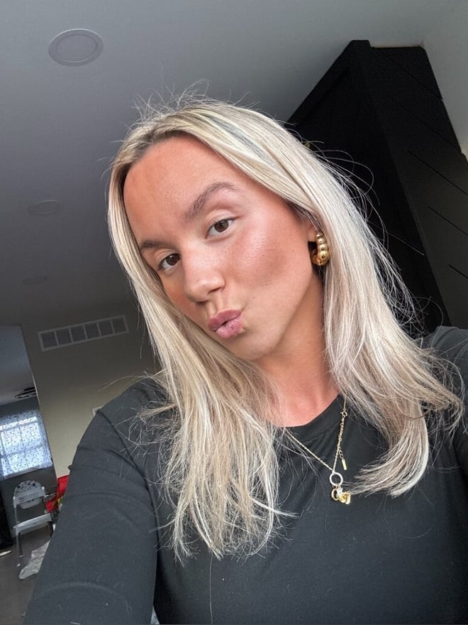 A close-up selfie of a blonde woman with hoop earrings making a playful expression indoors.
