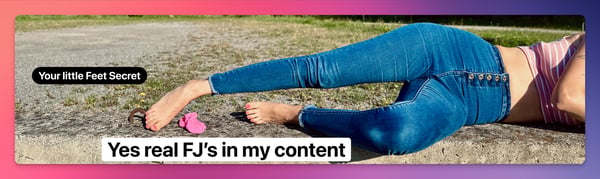A woman lying on the ground in blue jeans and a colorful top, posing with her bare feet extended towards the camera against an outdoor grassy background.