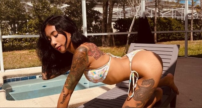 A tattooed woman in a floral bikini posing beside a swimming pool.