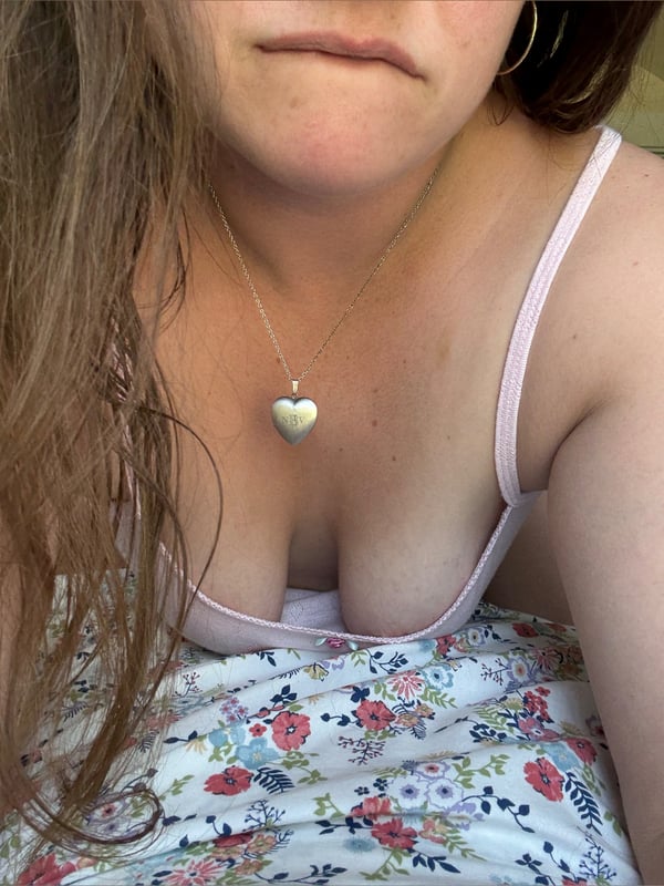 A woman with long brown hair wearing a pink tank top and floral skirt, posing outdoors with a necklace.