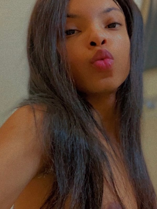 Young woman with long dark hair making a kissy face, smiling playfully in a casual indoor selfie.