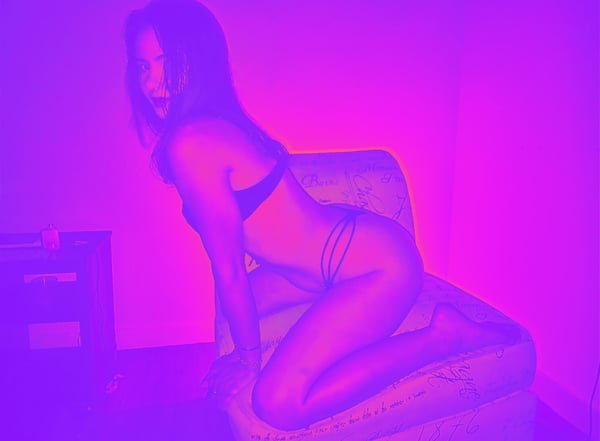 A woman posing on a chair in a dimly lit room with purple lighting and artistic effects.