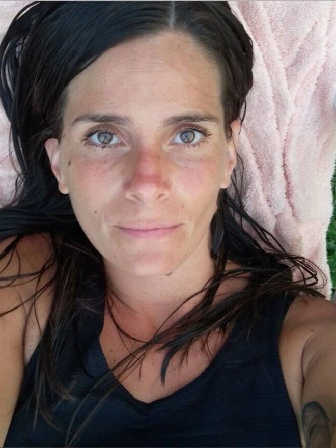 Close-up portrait of a woman with long dark hair and brown eyes lying down, smiling slightly.