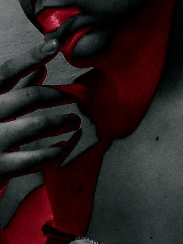 Black and white close-up of a woman's face with red lips, making a subtle gesture with her fingers.