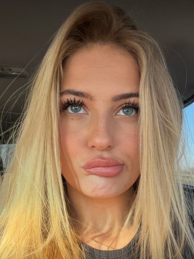Close-up portrait of a blonde woman seated in a car, looking at the camera.