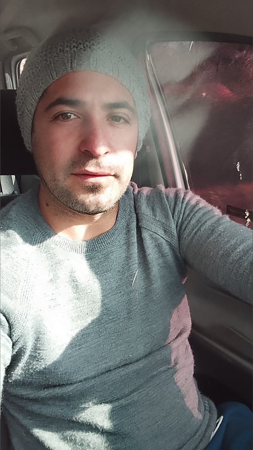 Man wearing a gray beanie and sweater, sitting in a car with sunlight streaming in.
