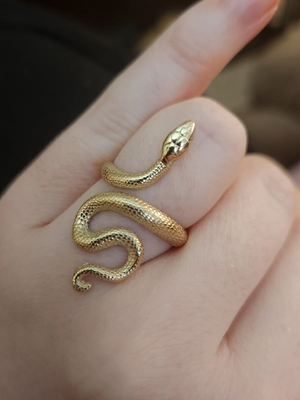 Close-up of a hand wearing an intricate gold snake ring coiled around the finger.