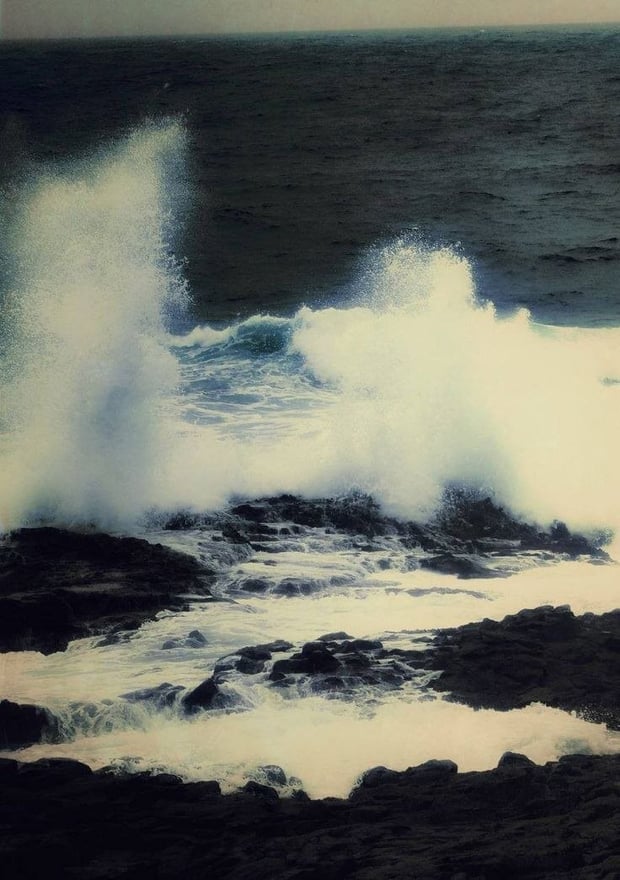 Ocean waves crashing against dark rocky shores under a muted sky.