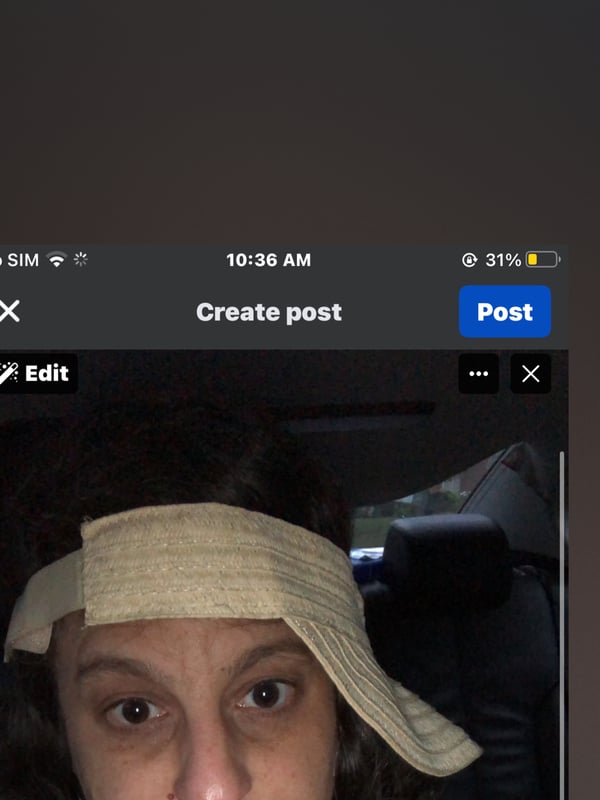A young woman with curly dark hair wearing a beige headscarf and black top, posing in a car.