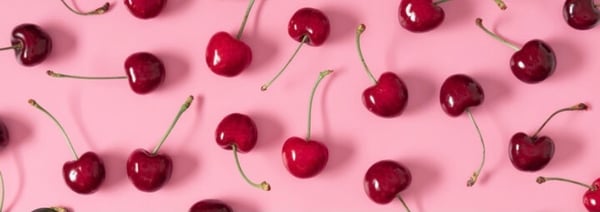 Close-up artistic arrangement of fresh red cherries scattered on a soft pink background.