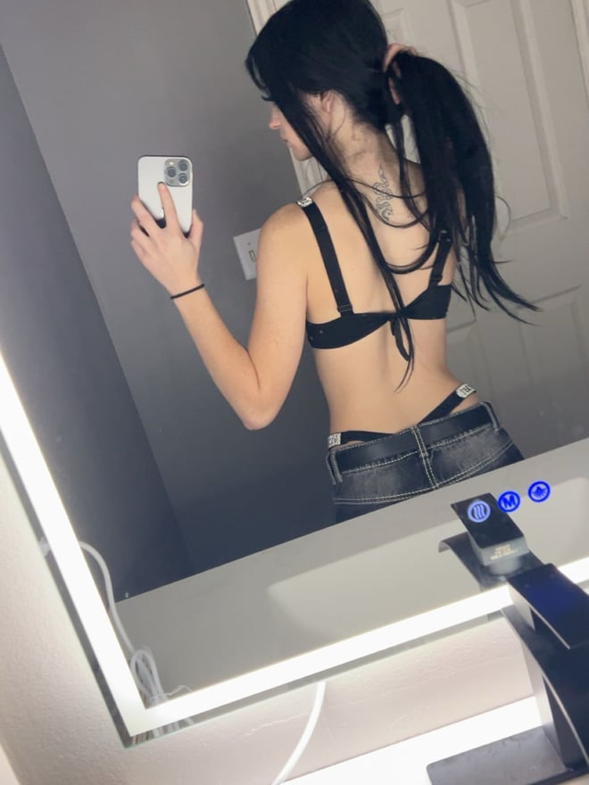 A young woman with long blue hair posing for a mirror selfie in a checked top.