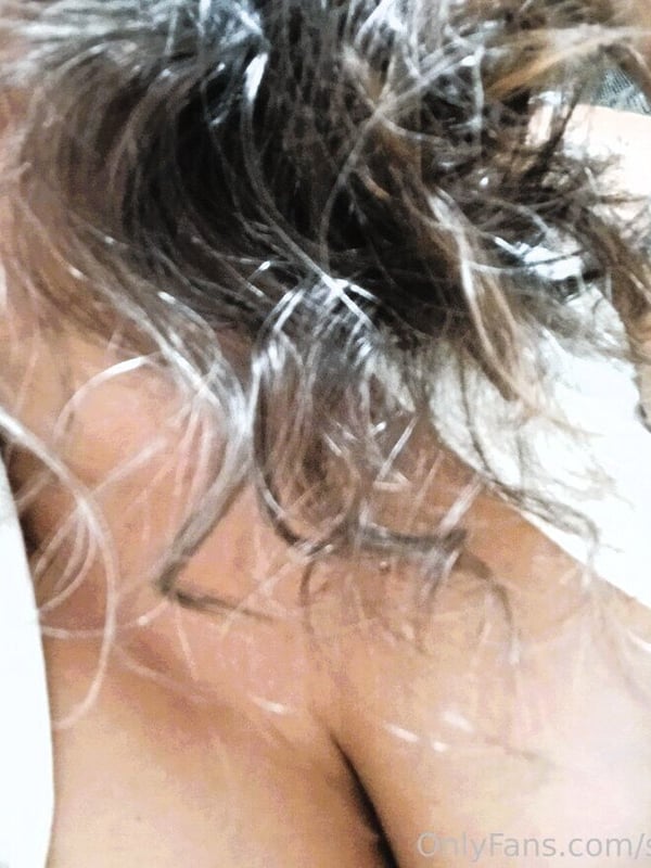 Close-up portrait of a smiling woman with wavy brown hair and white top.