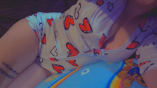 A woman lounging on a blue inflatable float in a heart-patterned onesie, with tattoos visible on her leg.