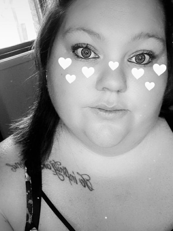 Close-up portrait of a woman with dark hair in pigtails wearing cute black bows, adorned with heart-shaped filters over her eyes, smiling playfully.