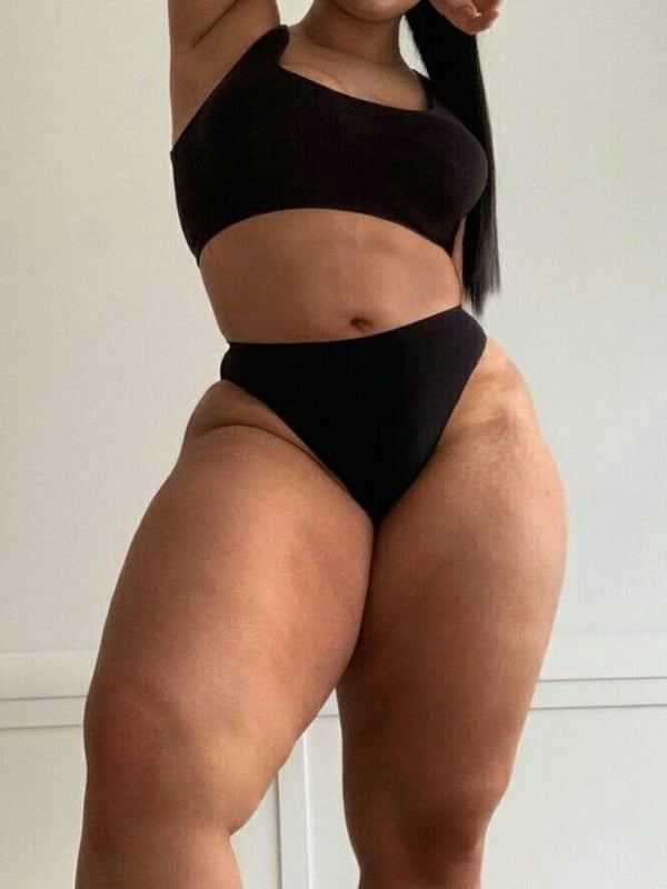 A curvy woman poses confidently in a black top and bottoms against a plain background.