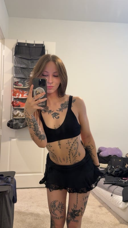 A woman with long brown hair posing in black underwear in a bathroom setting.