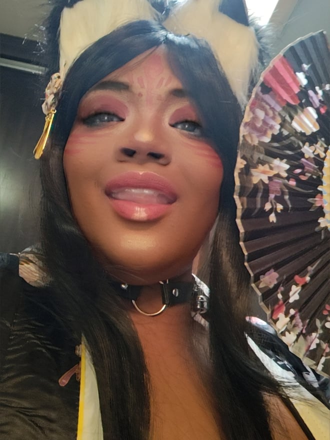 A woman in cosplay attire with cat ears, choker, and a fan, posing with dramatic makeup.