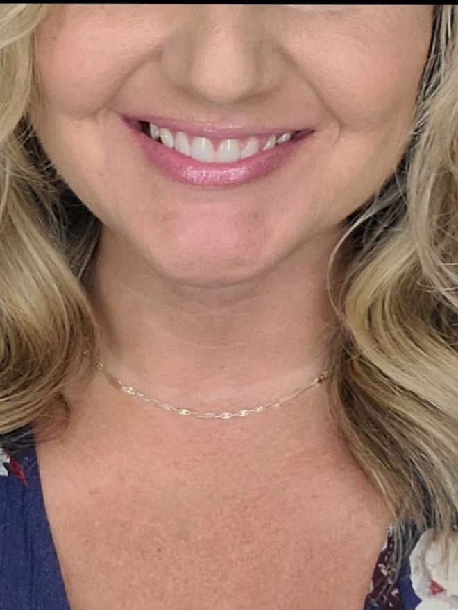 Close-up portrait of a smiling blonde woman with wavy hair, wearing a delicate necklace.