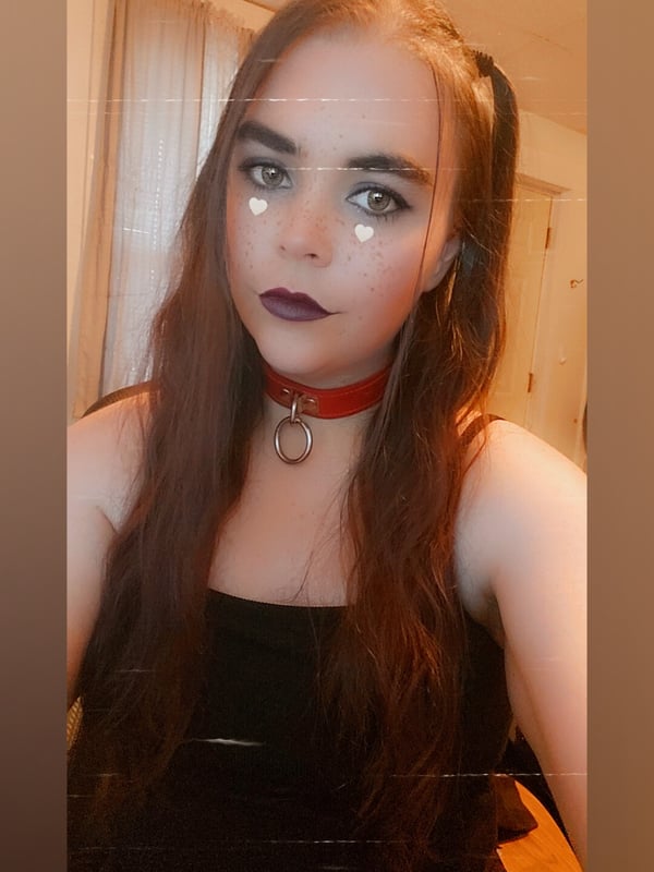 Young woman with long brown hair in pigtails and a choker necklace, posing with dramatic makeup indoors.