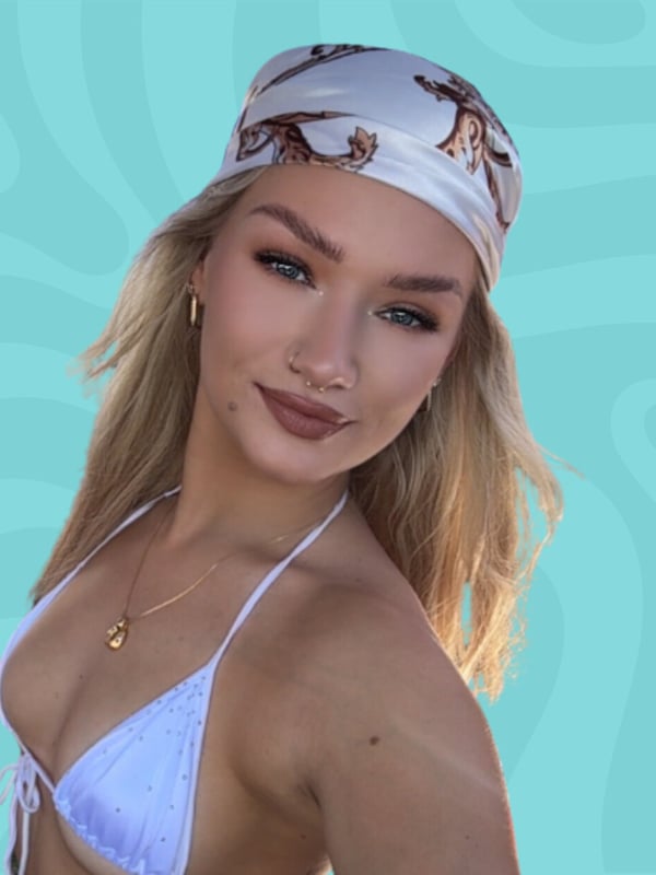 A young woman with long blonde hair wearing a white bikini top and headscarf, smiling against a blue background.