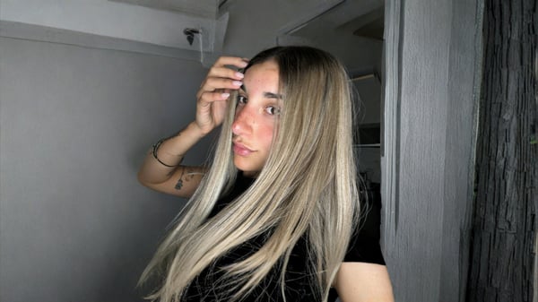 A young woman with long blonde hair posing indoors near a doorway.
