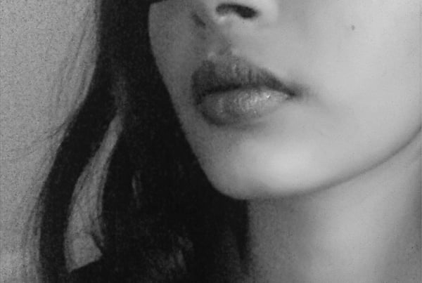 Close-up portrait of a woman with dark hair, featuring her lips and facial profile in black and white.