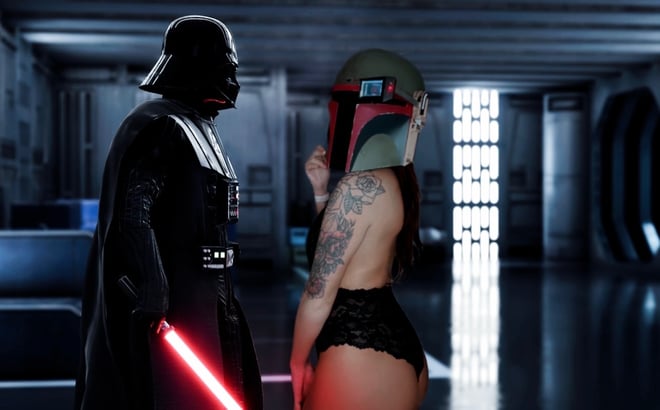 A woman in black lingerie and a Mandalorian helmet posing next to Darth Vader holding a lightsaber in a futuristic corridor setting.