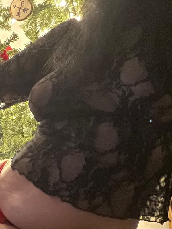 A woman posing in lace attire near a decorated Christmas tree with festive ornaments.