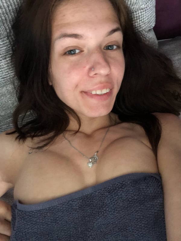 A young woman with brunette hair smiling while lying on a couch, wrapped in a towel.