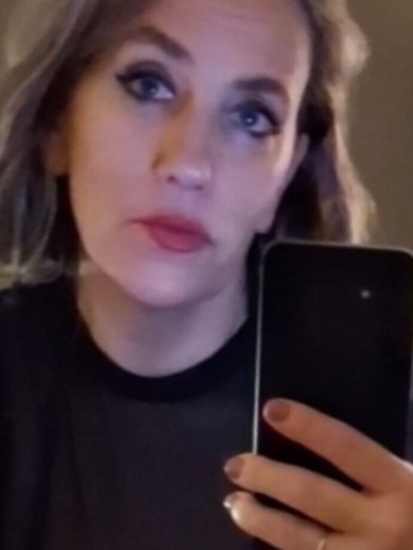 Woman with wavy hair and blue eye makeup taking a selfie while holding a phone.