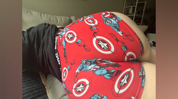 Person lounging on a couch wearing themed red underwear with Captain America designs and a dark shirt.