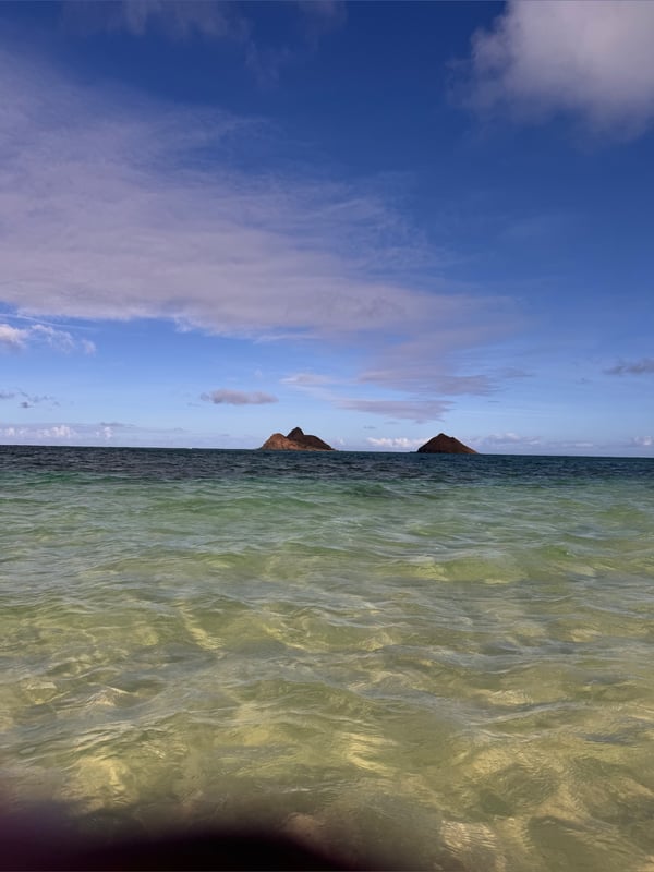 Scenic ocean view with two small islands under a partly cloudy blue sky.
