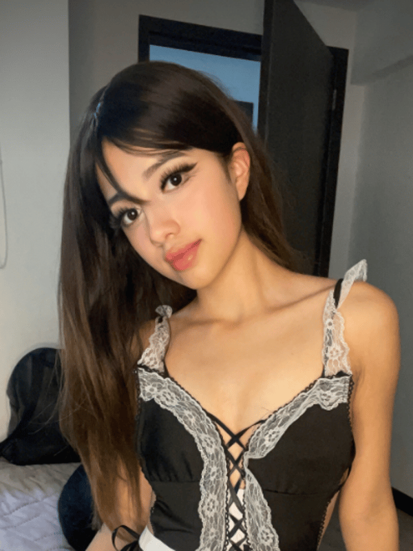 A person with long dark hair wearing a black lace top, posing indoors.
