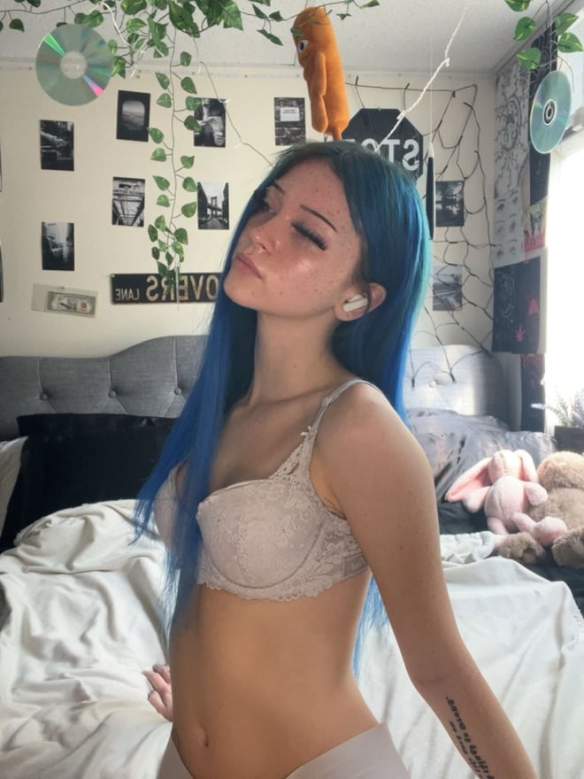 A young woman with long blue hair posing for a mirror selfie in a checked top.