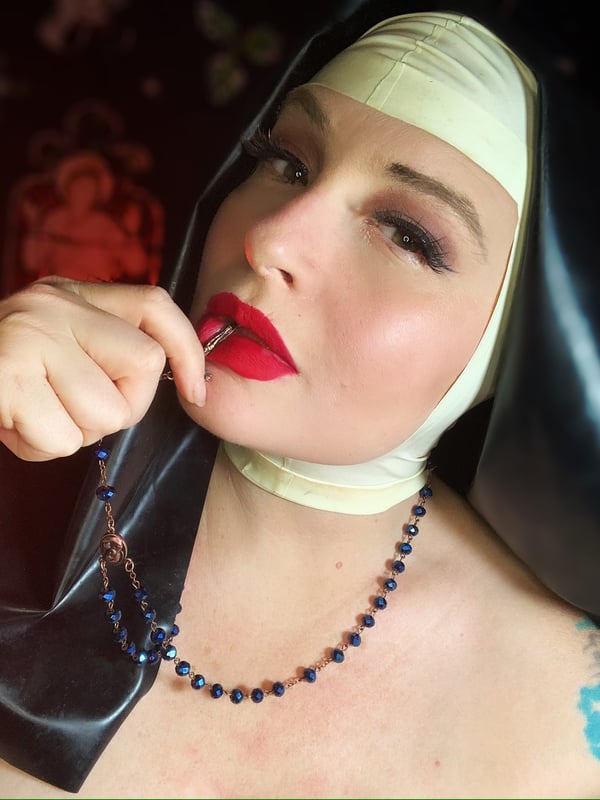 Woman in nun costume with red lipstick and beads, posing seductively.